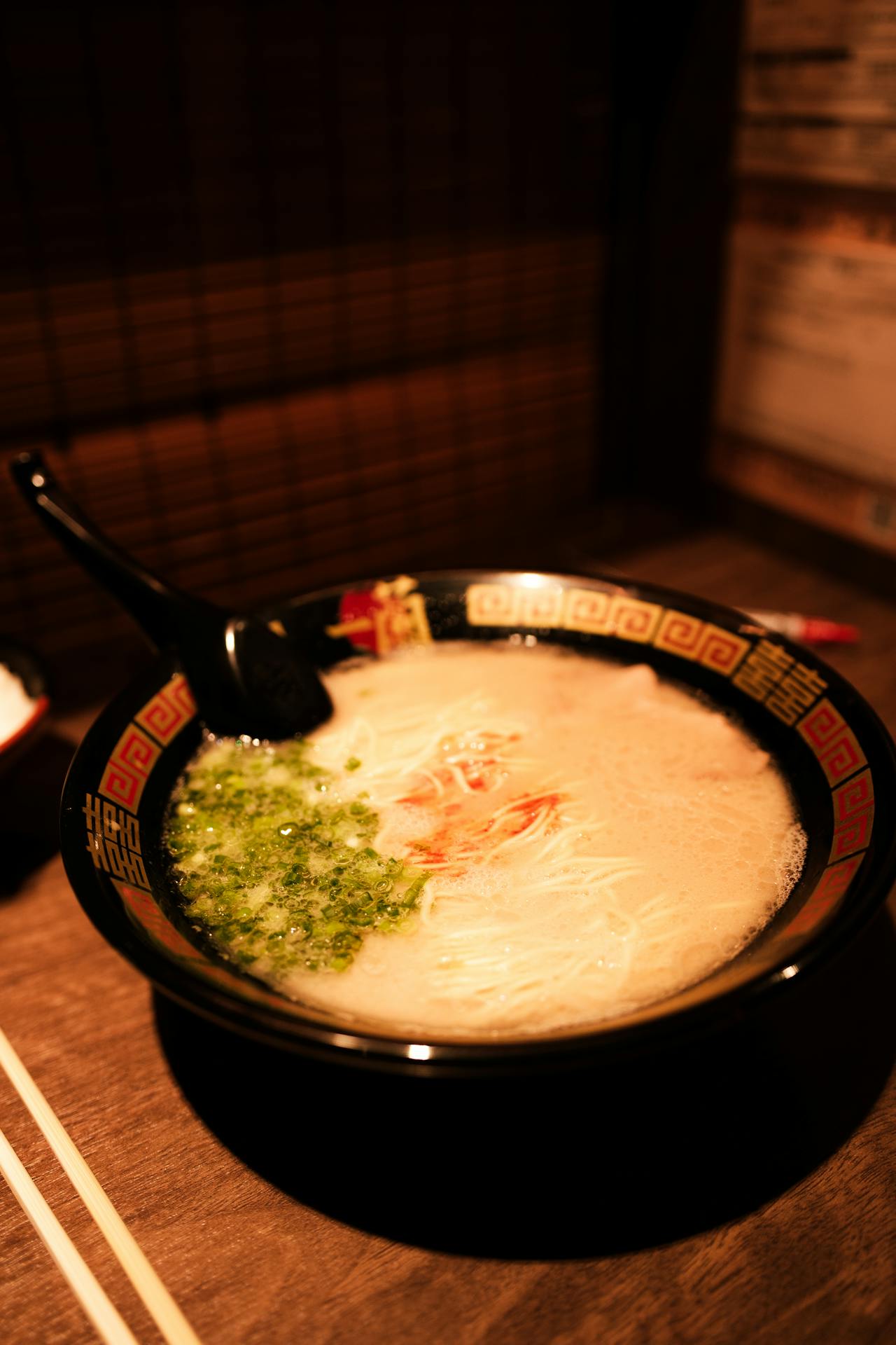 Close-up of an Ichiran tonkotsu ramen bowl showing thin noodles, chopped green onion and the signature red secret sauce in creamy pork broth