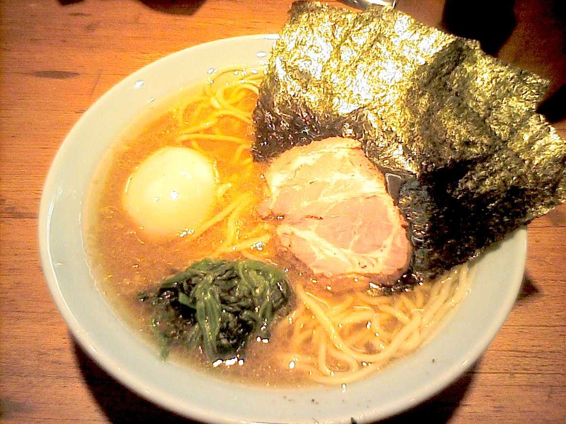 A close-up of iekei ramen — glossy soy-tonkotsu broth, thick noodles, spinach, standing sheets of nori and char siu