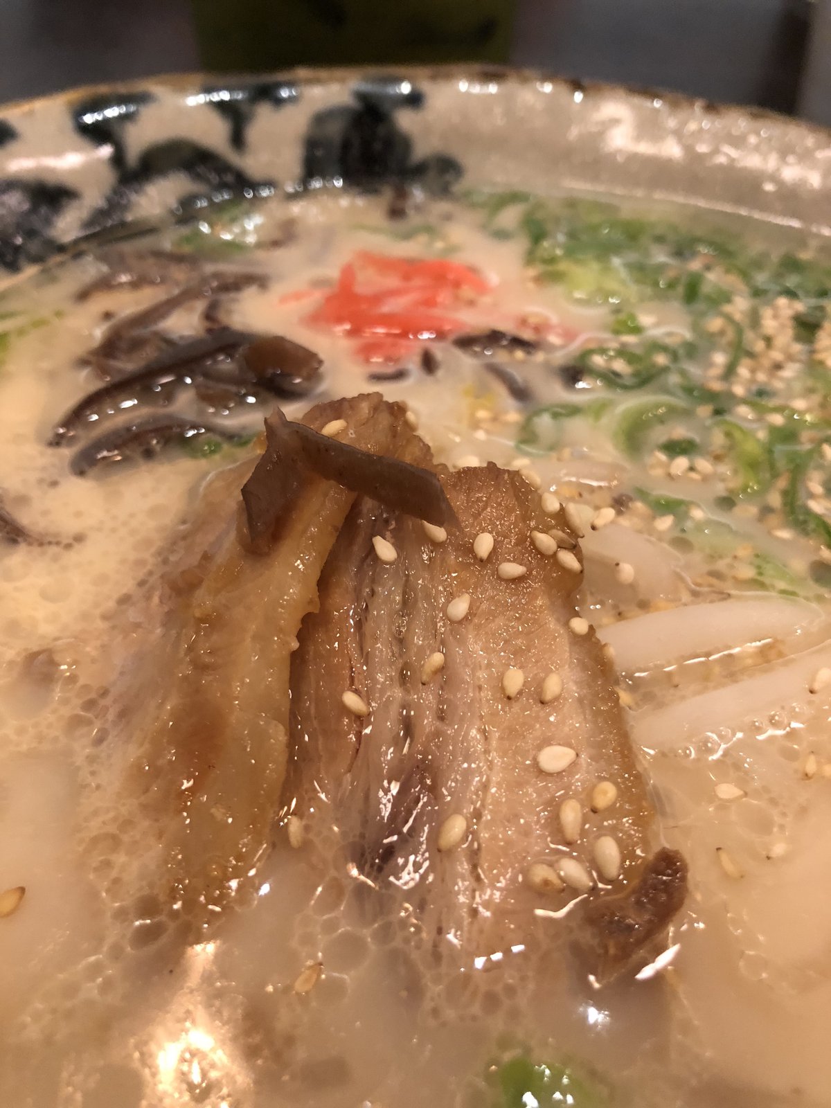 A close-up of milky-white Hakata tonkotsu ramen with extra-thin straight noodles, wood-ear mushroom, spring onion and char siu