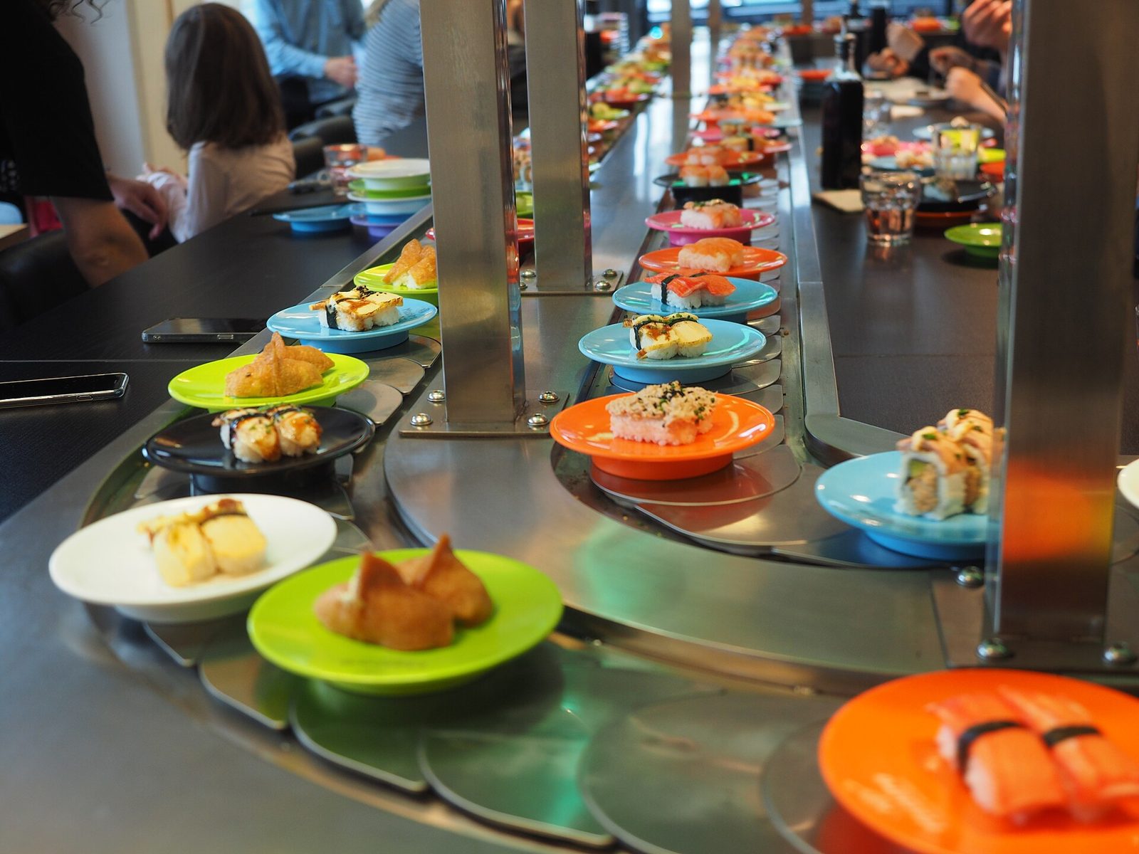 Colourful plates of nigiri and rolls moving along the conveyor belt of a kaiten-zushi restaurant