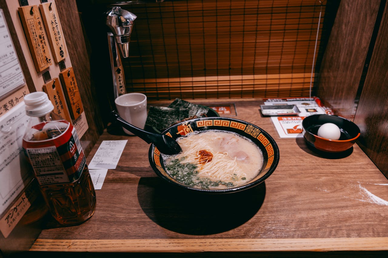 An Ichiran tonkotsu ramen bowl in its wooden solo booth, with the paper order sheet and a small egg dish for the kaedama noodle refill