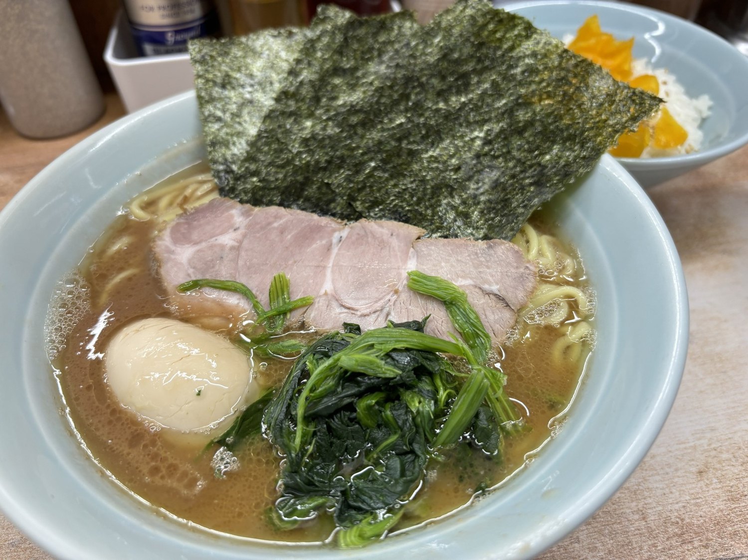 A hearty bowl of Musashiya iekei ramen — soy-tonkotsu broth, thick noodles, spinach, a soft egg, char siu and sheets of nori, with a bowl of rice and takuan
