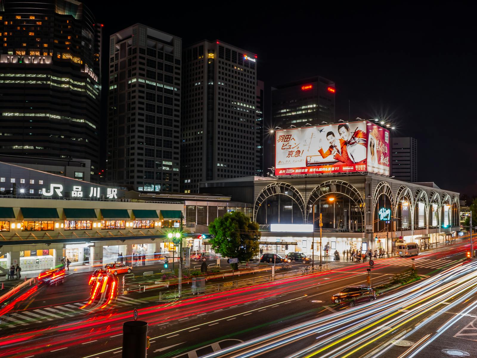 JR Shinagawa Station lit up at night with skyscrapers behind and traffic light trails